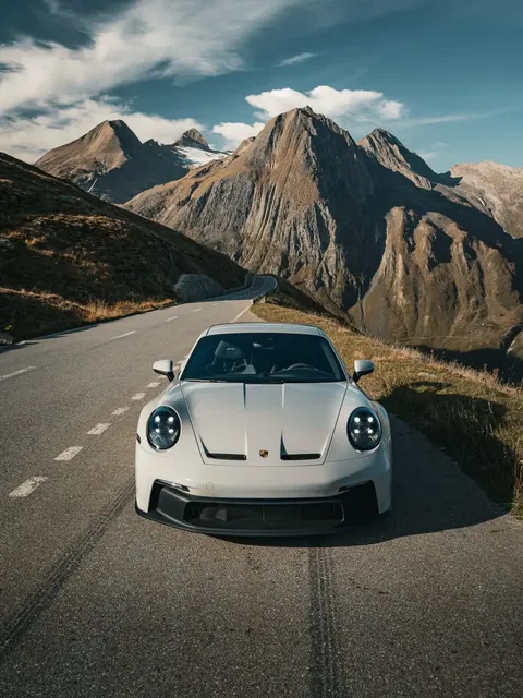 Silberner Porsche 911 GT3 auf einer kurvigen Bergstraße zwischen steilen Gipfeln
