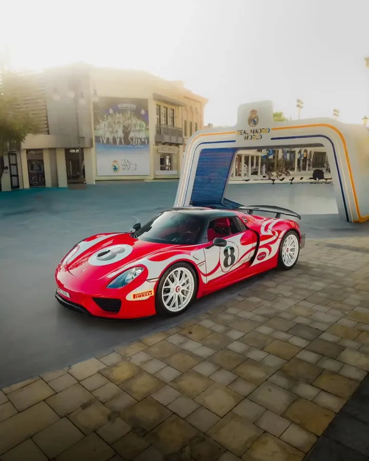 Rot-weiß gestalteter Porsche 918 Spyder mit Startnummer 8 und weißen Rädern vor einem Eingangsportal
