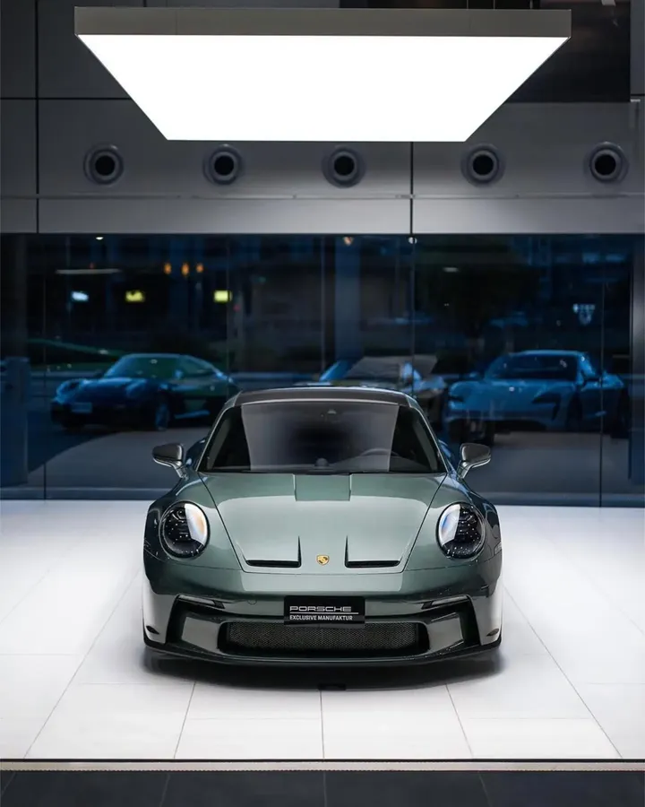 Grüner Porsche 911 GT3 Touring in Frontansicht unter einer großen Leuchtfläche im Ausstellungsraum