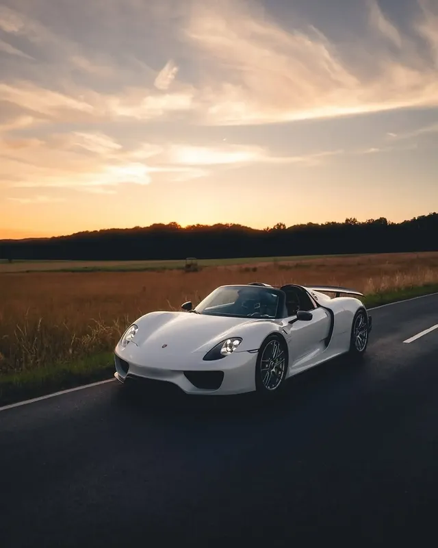 Weißer offener Porsche 918 Spyder auf einer Landstraße vor Feldern im Abendlicht