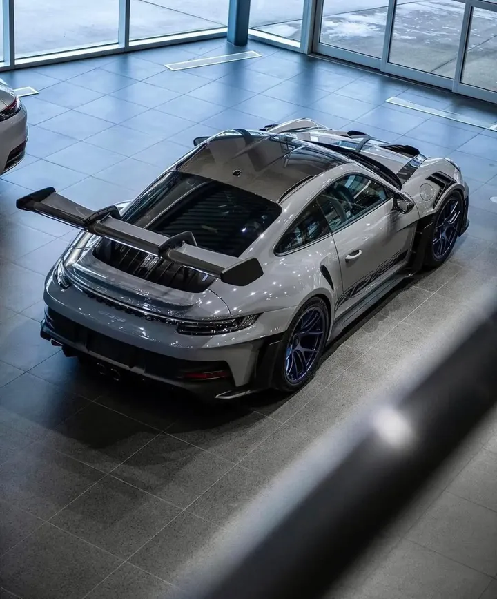 Grauer Porsche mit großem Heckflügel und dunklem Dach aus erhöhter Heckperspektive in einer Ausstellungshalle