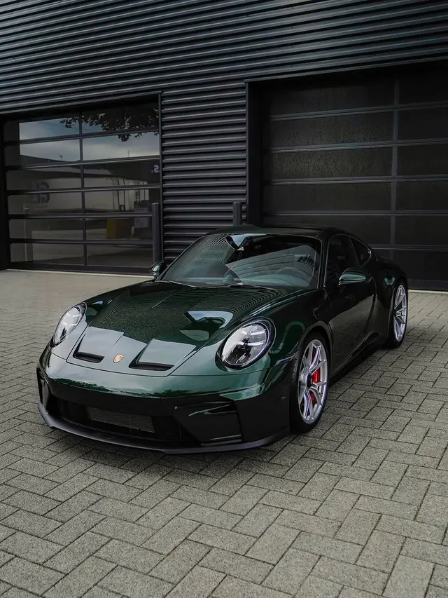 Dunkelgrüner Porsche 911 vor dunklen Hallentoren in schräger Frontansicht