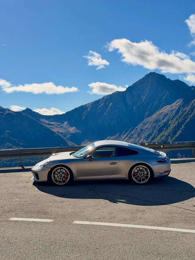 Silberner Porsche 911 GT3 Touring in Seitenansicht am Jaufenpass vor einer Bergkulisse. Originalfoto von @my_gt3touring.