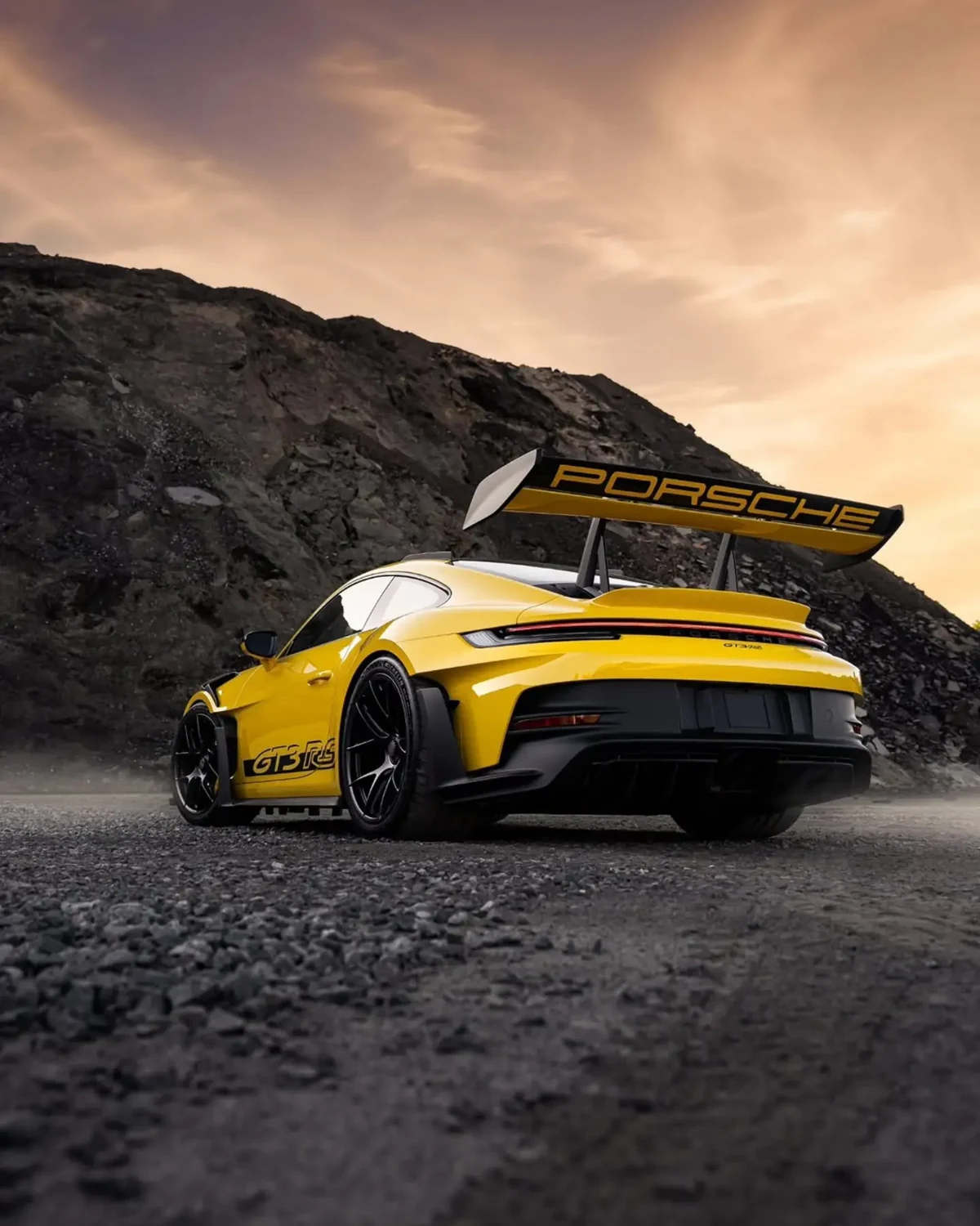 Gelber Porsche 911 GT3 RS in Heckansicht vor felsiger Landschaft und warmem Abendhimmel. Foto: @mikekuhnracing.