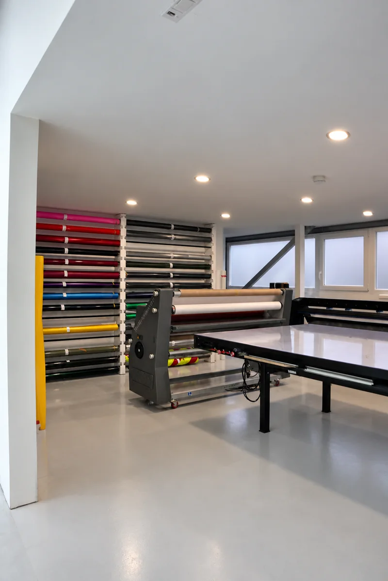 Folienlager bei GLAXI mit farbigen Folienrollen, Laminator und Arbeitstisch.