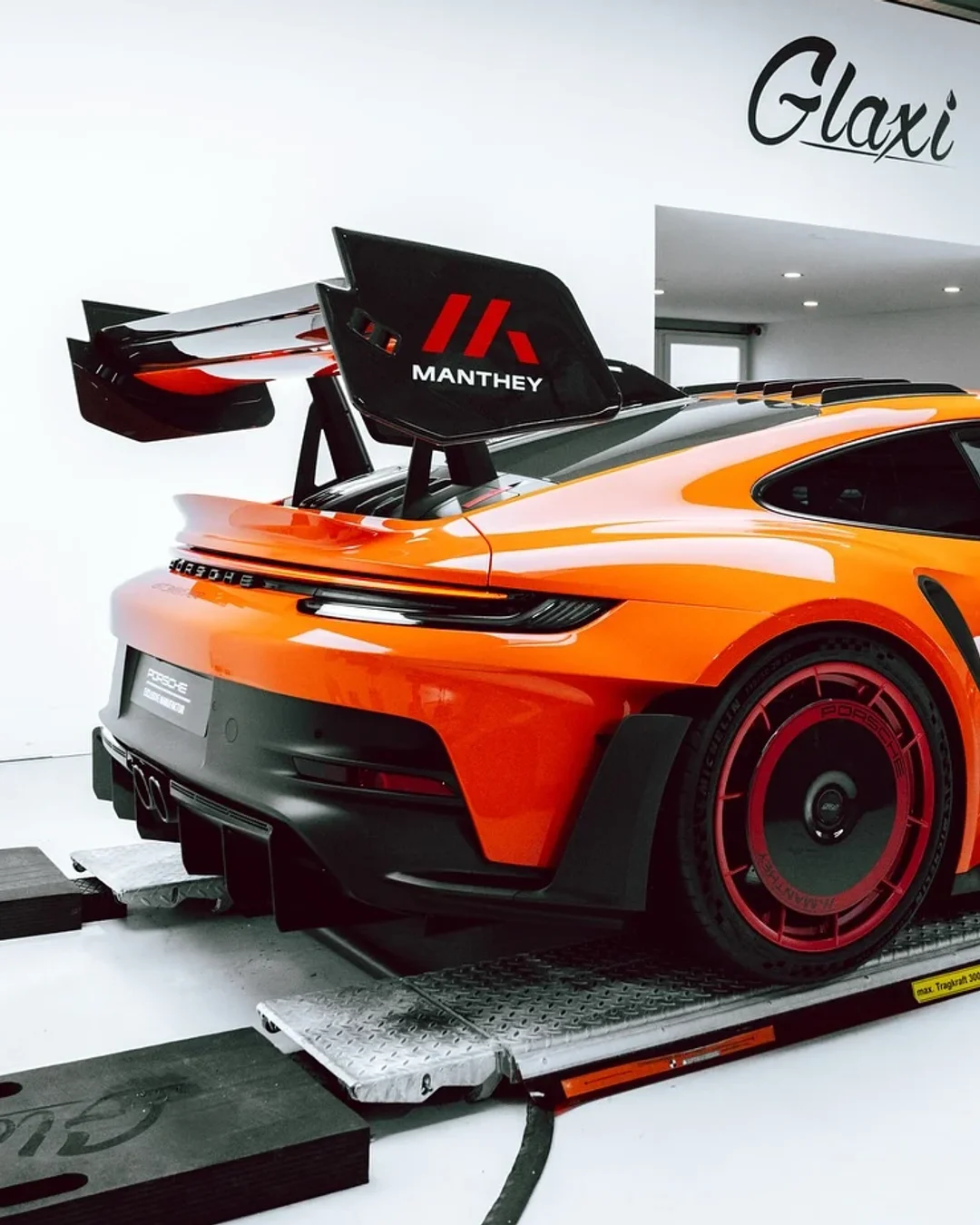 Orangefarbener Porsche 911 GT3 RS mit Manthey-Kit in der GLAXI-Manufaktur, von hinten fotografiert.