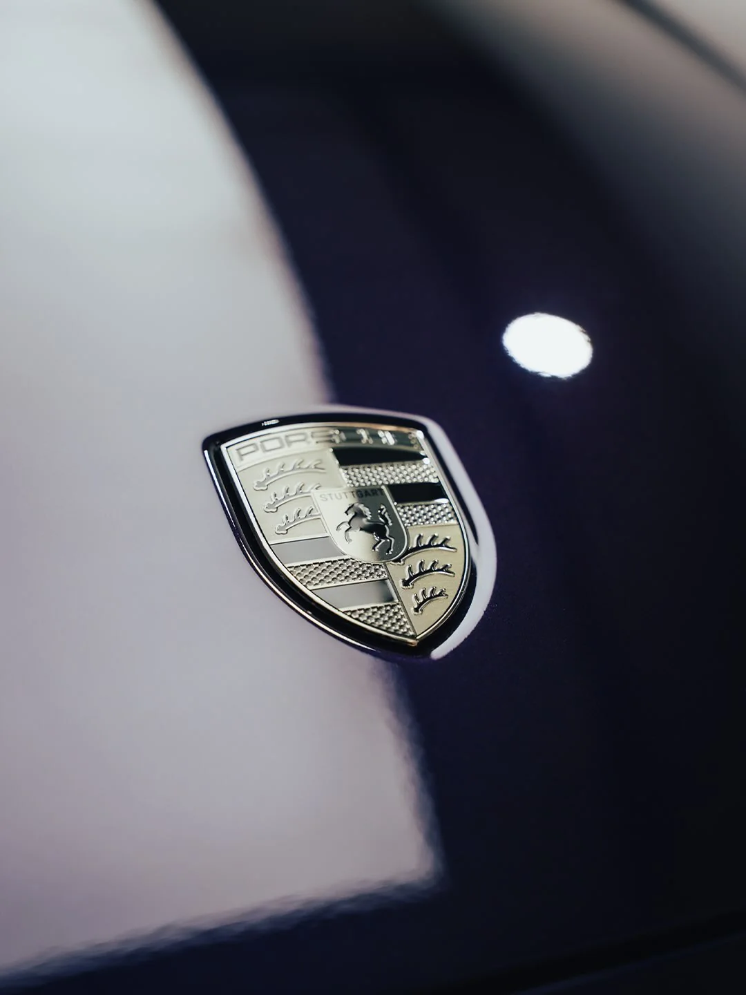 Porsche-Wappen und Reflexe der Hallenbeleuchtung auf der violetten Motorhaube des Porsche Turbo S