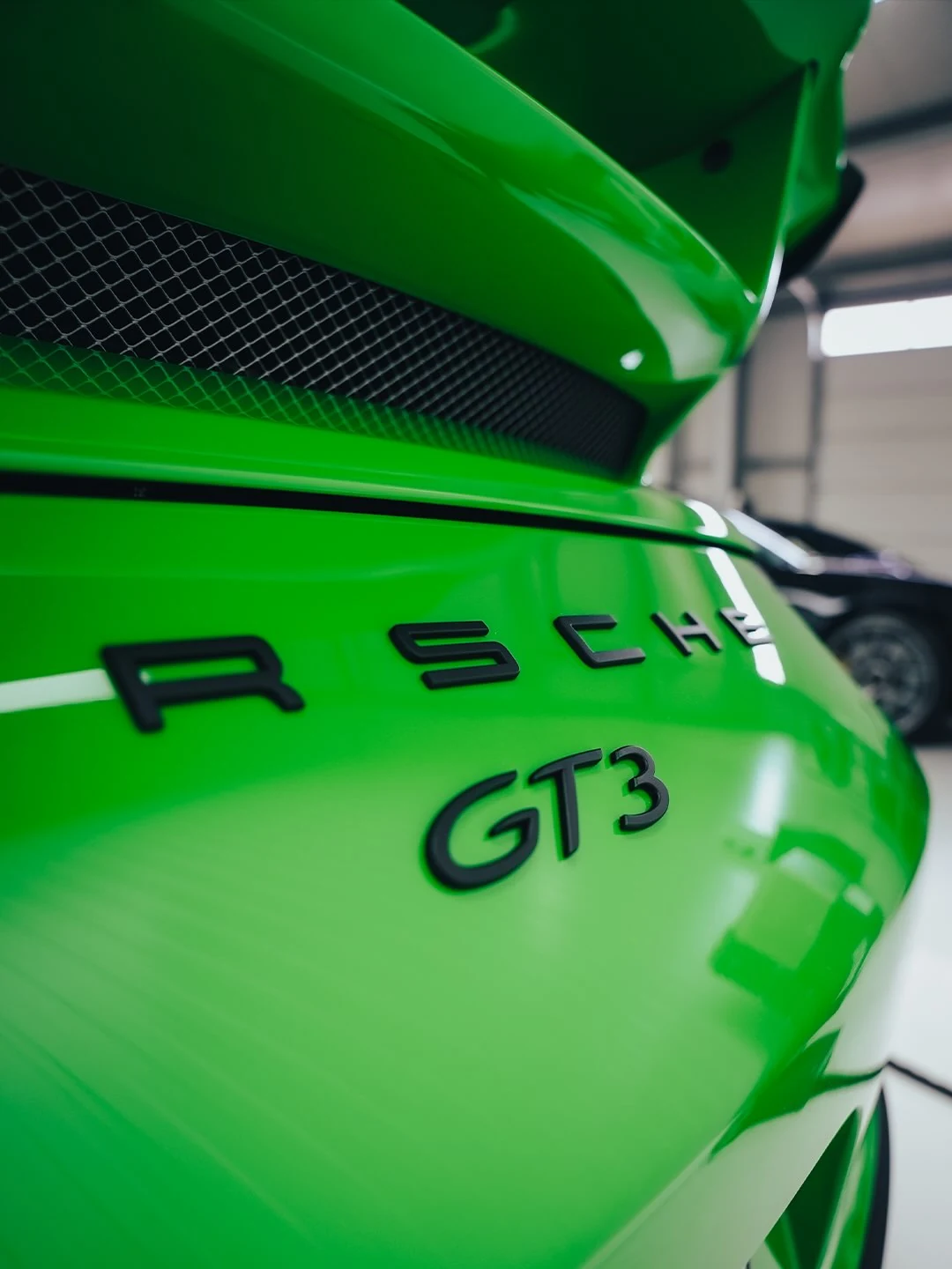 Nahaufnahme am Heck eines grünen Porsche 911 GT3 mit PORSCHE- und GT3-Schriftzug, Heckflügel und Lüftungsgitter