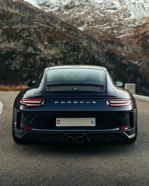 Heckansicht eines dunkelblauen Porsche 911 GT3 Touring vor einer Berglandschaft