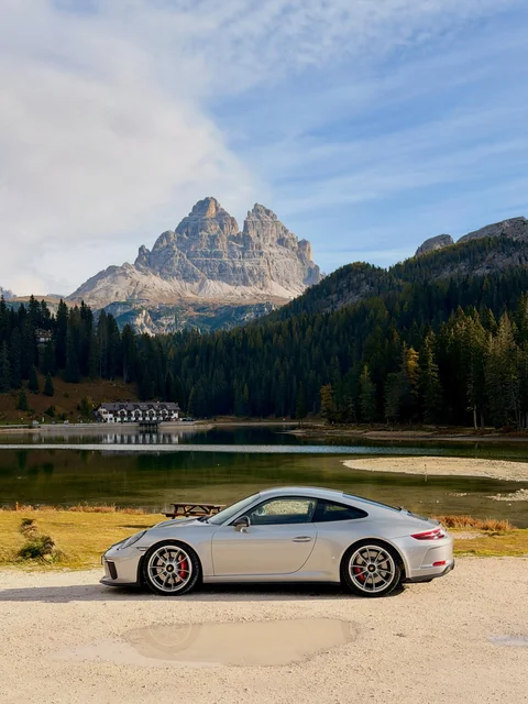 Silberner Porsche 911 GT3 Touring in Seitenansicht an einem Bergsee vor dem Dolomitenpanorama