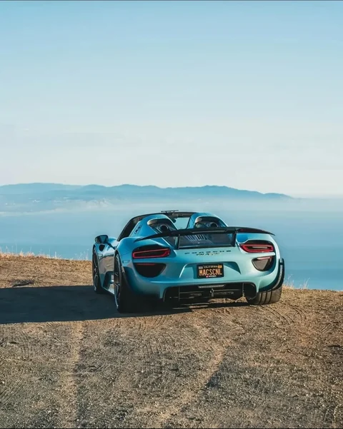 Hellblauer Porsche 918 Spyder in Heckansicht auf einer Küstenstraße mit Blick auf das Meer. Foto: @c.j.n.photography.