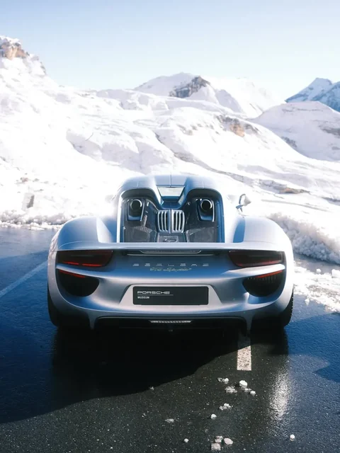 Silberner Porsche 918 Spyder von hinten auf einer Straße vor schneebedeckten Bergen. Foto: @samkoza.