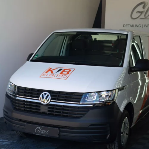 Es ist eine Flottenbeschriftung auf einem VW T6 in grau und orange zu sehen. Man sieht, das es Folie ist, da man es so nie lackieren könnte. Kleine Schriften auf dem Fahrzeug zeigen, dass es von der Firma KB Elektro GmbH in Schwäbisch Hall ist.