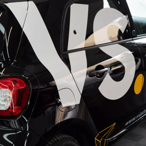 Mehrere Firmenlogos auf einem Auto, Folie auf den Lack geklebt, darunter ein Glaxi Logo. Der Lack glänzt. Fahrzeugbeschriftung