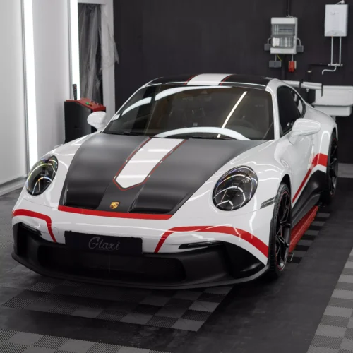 Das Bild zeigt einen Porsche 911 992 GT3 mit Designstreifen in rot. Zuvor wurde der Wagen mit Lackschutzfolie foliert. Die Folie glänzt, da im Anschluss eine Keramikversiegelung aufgetragen wurde.