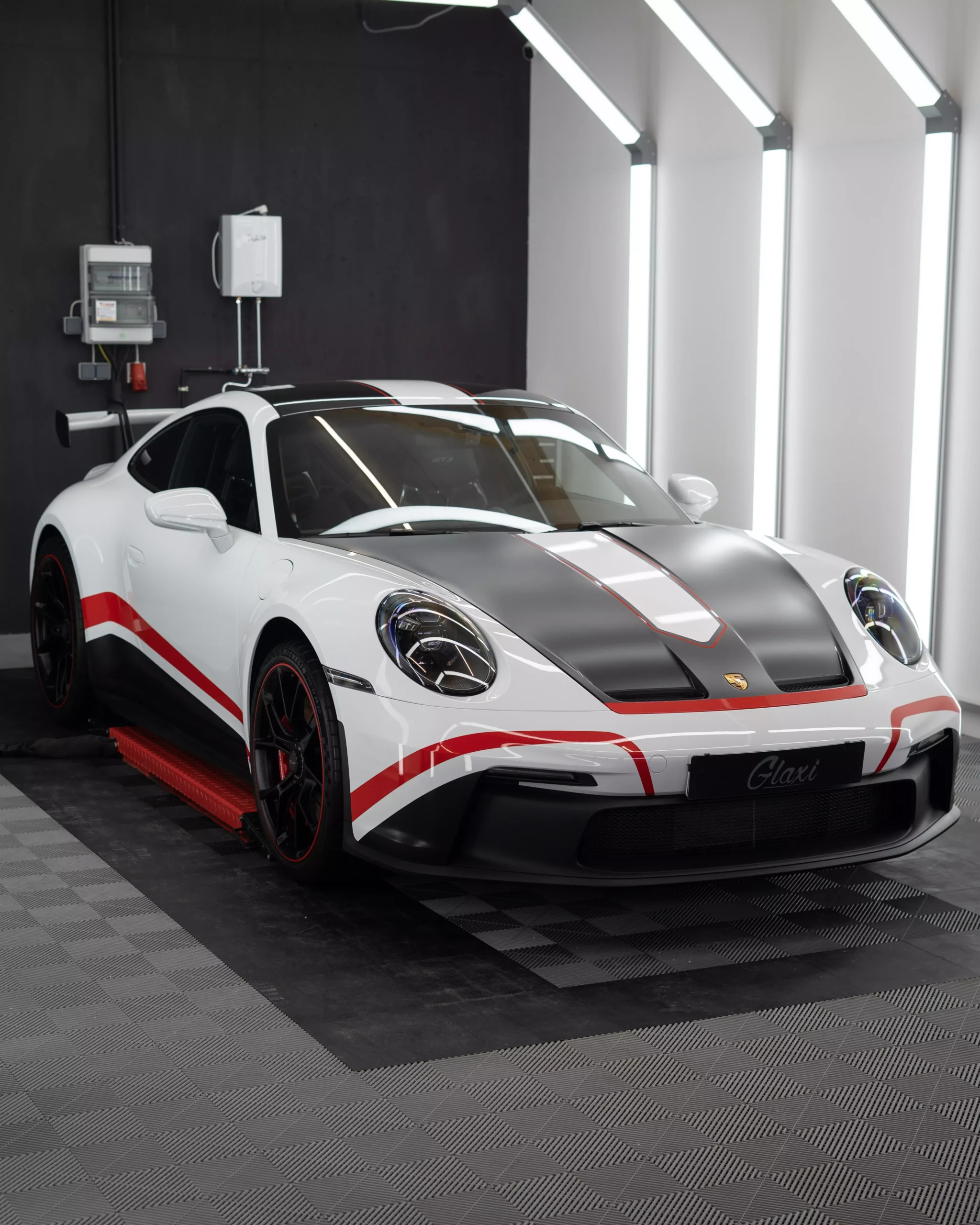 Das Bild zeigt einen Porsche 911 992 GT3 mit Designstreifen in rot. Zuvor wurde der Wagen mit Lackschutzfolie foliert. Die Folie glänzt, da im Anschluss eine Keramikversiegelung aufgetragen wurde.