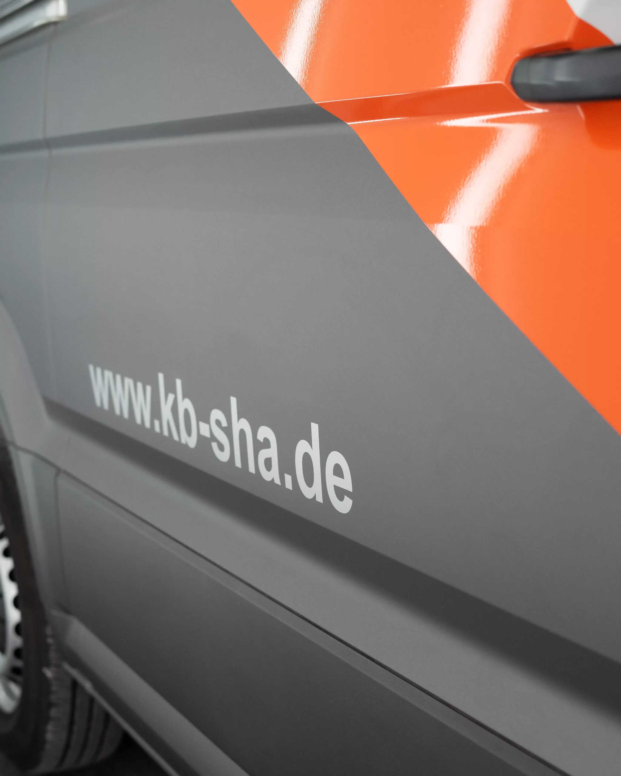 Es ist eine Flottenbeschriftung auf einem VW Crafter in grau und orange zu sehen. Man sieht, das es Folie ist, da man es so nie lackieren könnte. Kleine Schriften auf dem Fahrzeug zeigen, dass es von der Firma KB Elektro GmbH in Schwäbisch Hall ist.