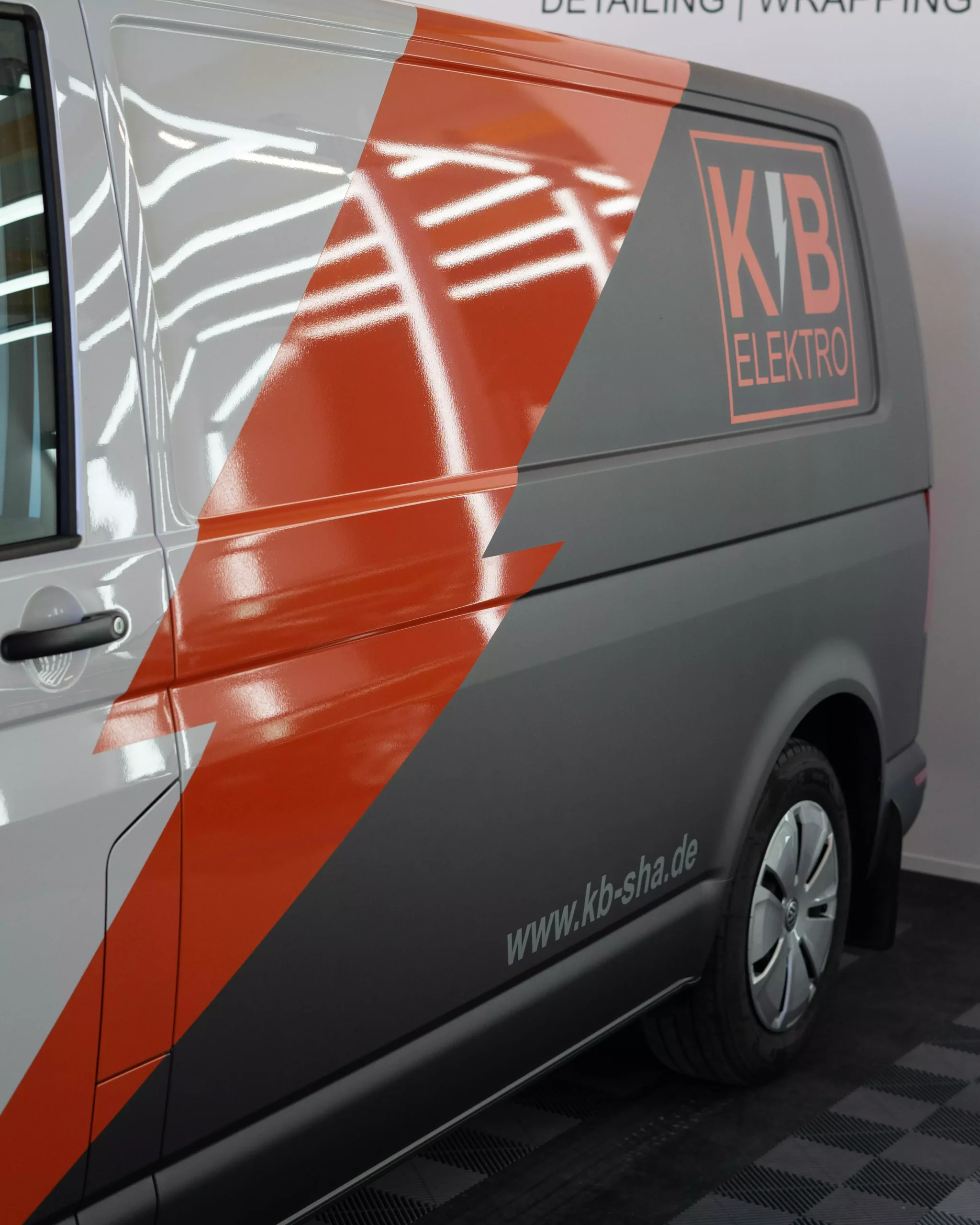 Es ist eine Flottenbeschriftung auf einem VW Crafter in grau und orange zu sehen. Man sieht, das es Folie ist, da man es so nie lackieren könnte. Kleine Schriften auf dem Fahrzeug zeigen, dass es von der Firma KB Elektro GmbH in Schwäbisch Hall ist.