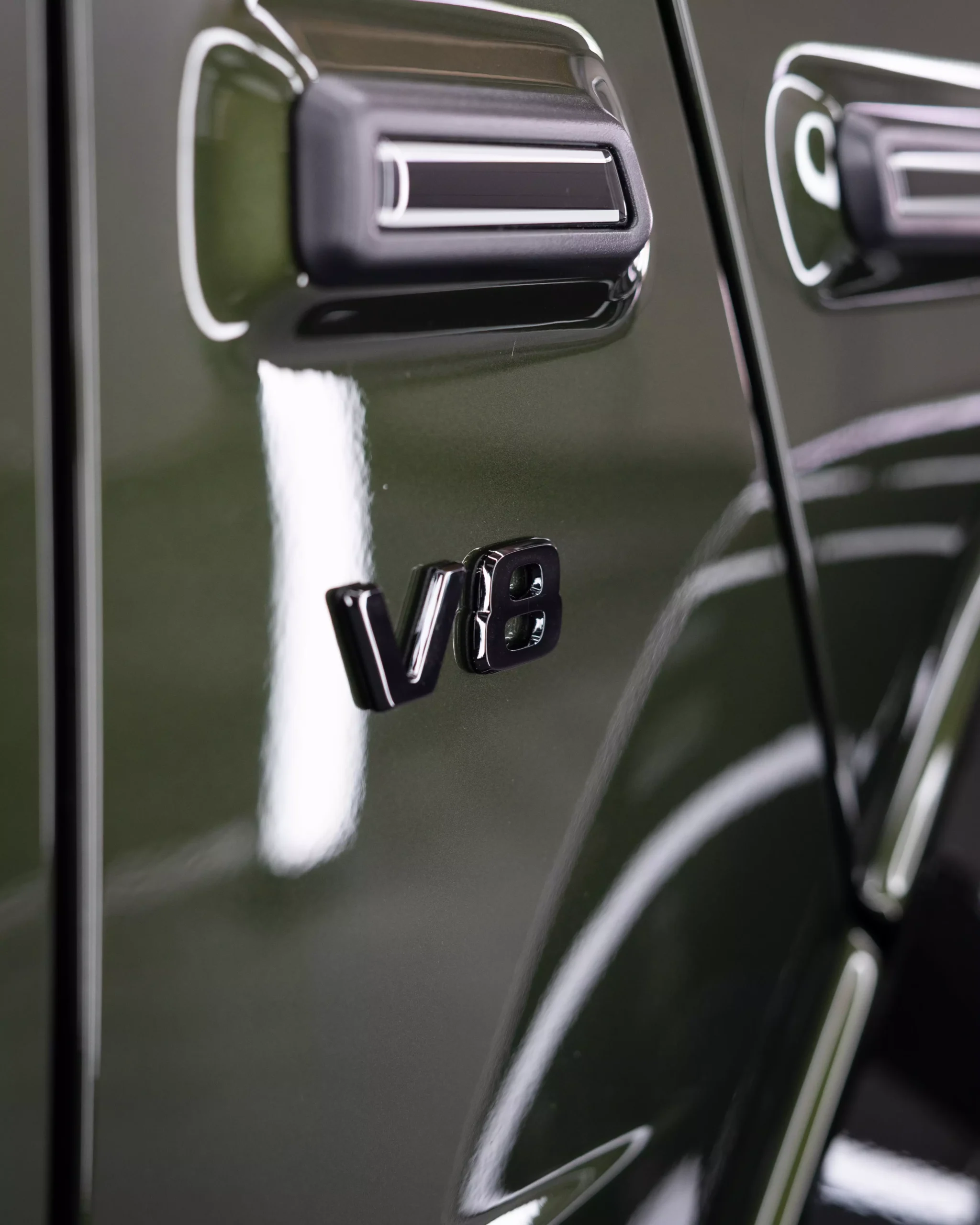 Glänzender, olivfarbener Lack nach der Lackpflege einer Mercedes G-Klasse. Kotflügel rechts mit schwarzem V8 Logo. Der Lack glänzt mit seiner Lackpflege und Keramikversiegelung.