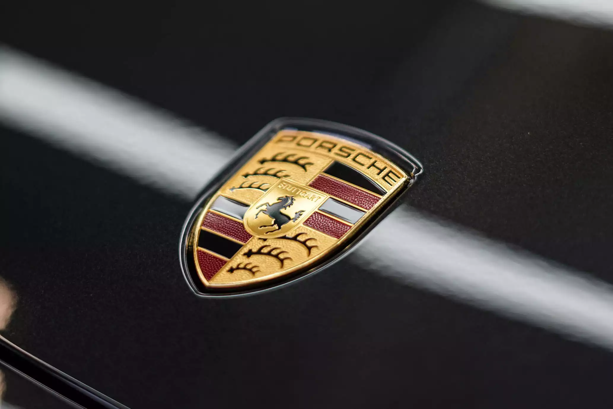 Porsche Logo auf grauer Motorhaube nach Lackpflege und Fahrzeugaufbereitung mit viel Glanz